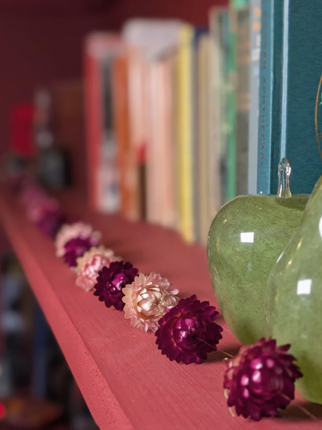 festive dried flower bud garland. pink dried flower garland laid on pink mantelpiece.