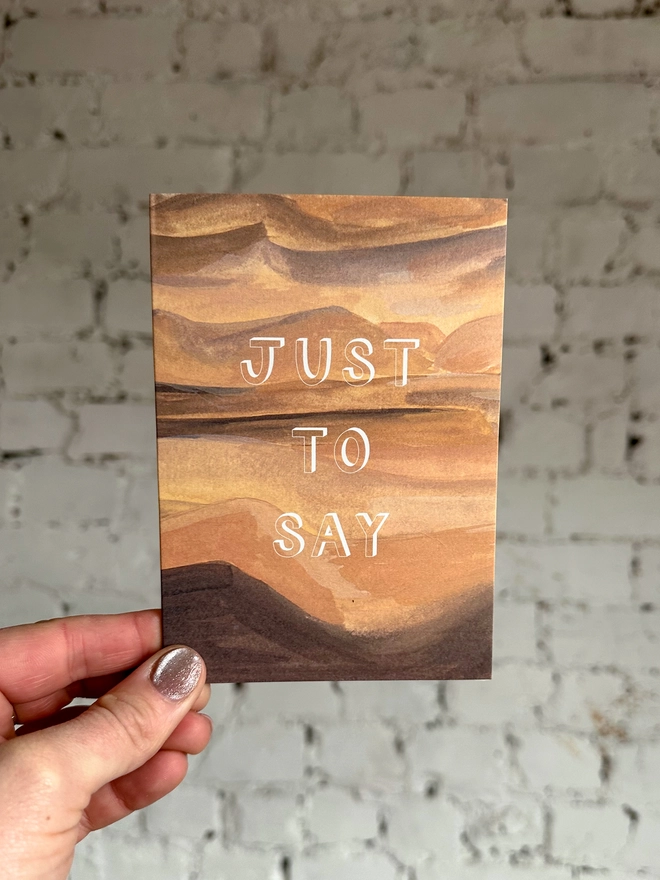 a greetings card featuring an illustration of a sand dunes landscape with the text “just to say”