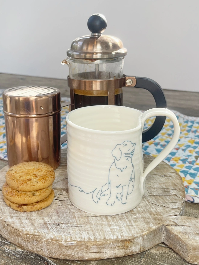 hand thrown porcelain mug with retriever line image on side in blue amidst coffee scene on rustic table