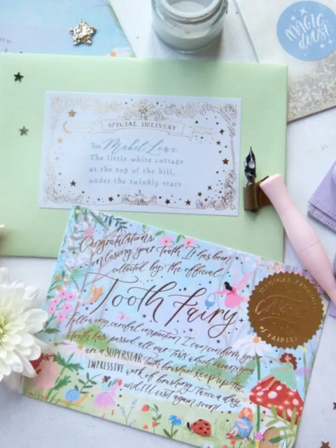 The garden notecard praises a "superstar tooth brusher" in gold foil calligraphy. Behind it is a green envelope addressed to Mabel Love, with a pink dip pen resting on it.