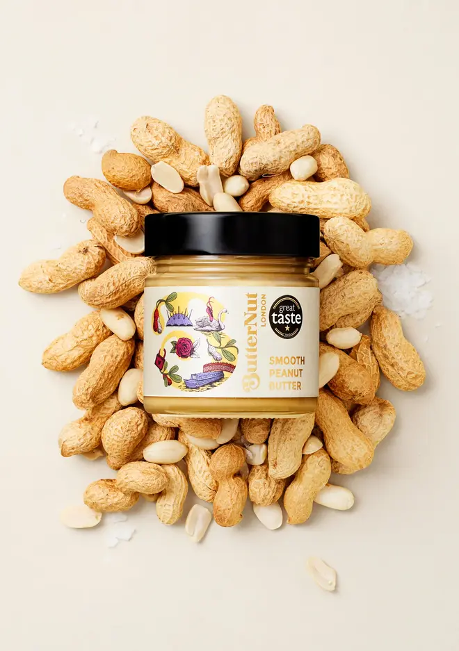 smooth peanut butter. a jar of peanut butter photographed against a beige background surrounded by peanuts.
