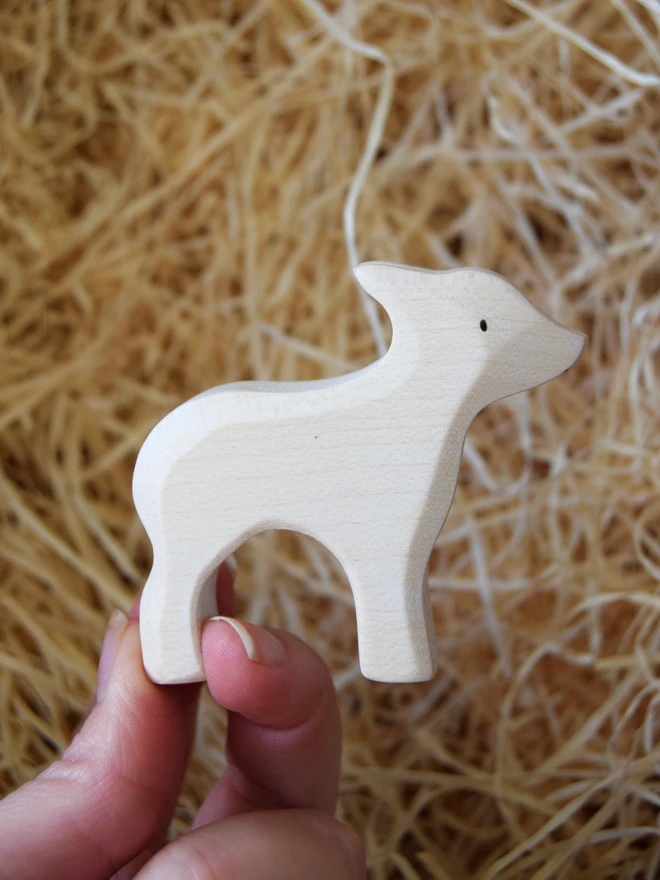 white lamb standing wooden toy held in hand above woodwool