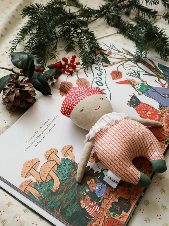 Soft handmade mushroom-themed doll with a red spotted cap, embroidered smiling face, ruffled white collar, red-striped body, and small green feet.