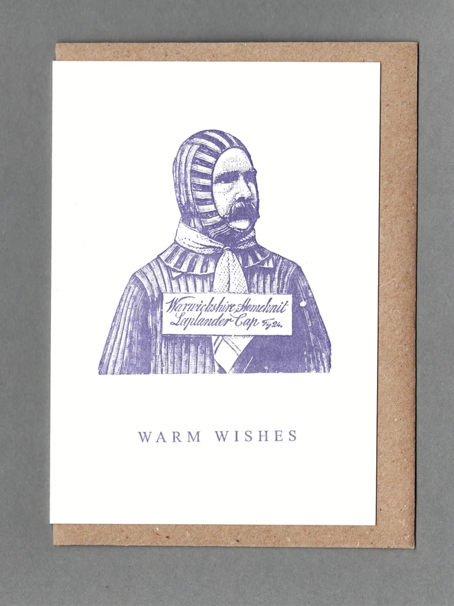 White card with purple illustration of a man in a balaclava with text reading 'Warm Wishes' with a brown envelope behind