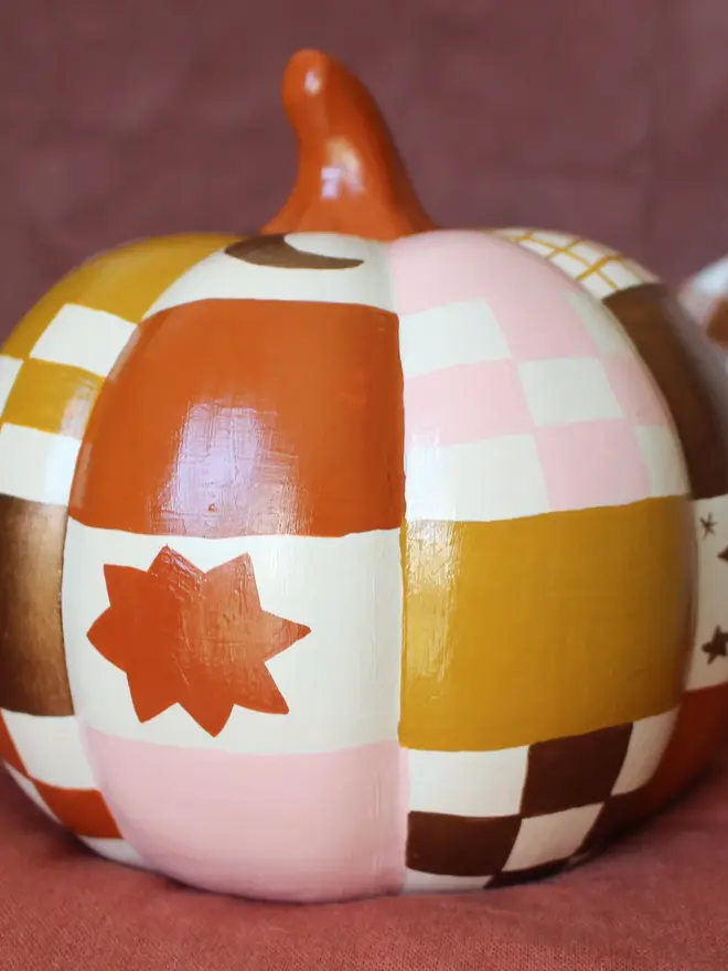 hand-painted celestial patchwork ceramic pumpkin. a ceramic pumpkin painted with patchwork colours of gold, pink, brown and stars and moons.