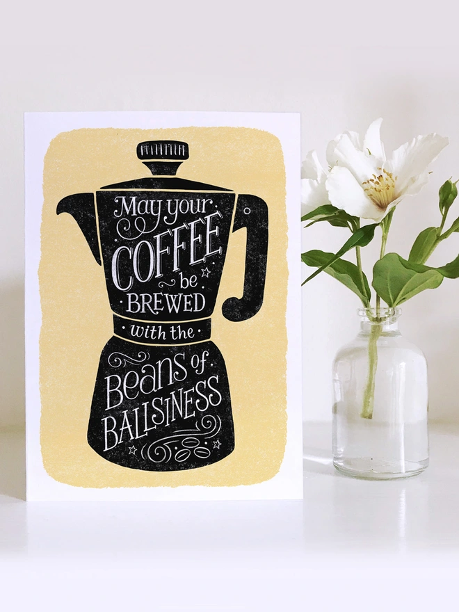 black coffee cup on yellow background with white hand lettered coffee quote inside with white flower in glass vase