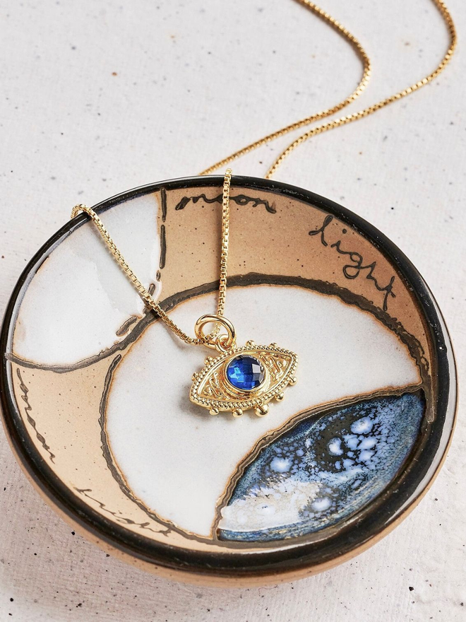 a gold evil eye charm necklace with a blue quartz stone on a gold box chain necklace