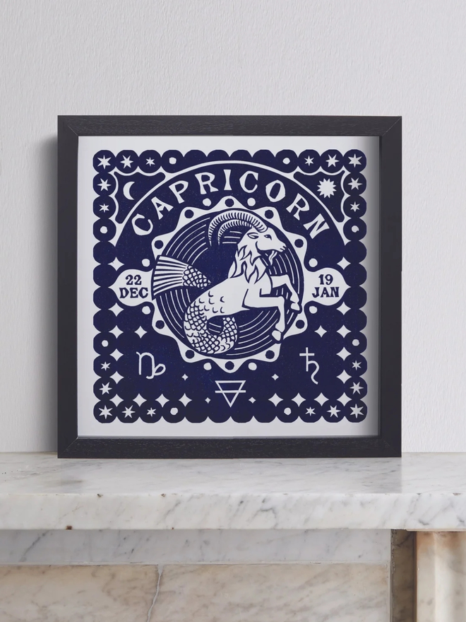 capricorn zodiac linocut. a linocut goat and zodiac symbols printed on a blue background.