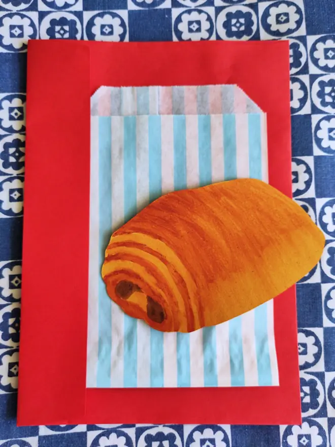 hand painted pain au chocolat, cut out paper shape. with blue and white striped paper bag and red envelope