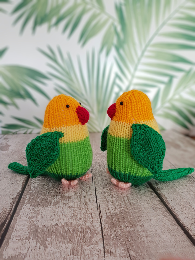 knitted lovebirds sitting on a wooden floor with palm trees in the background