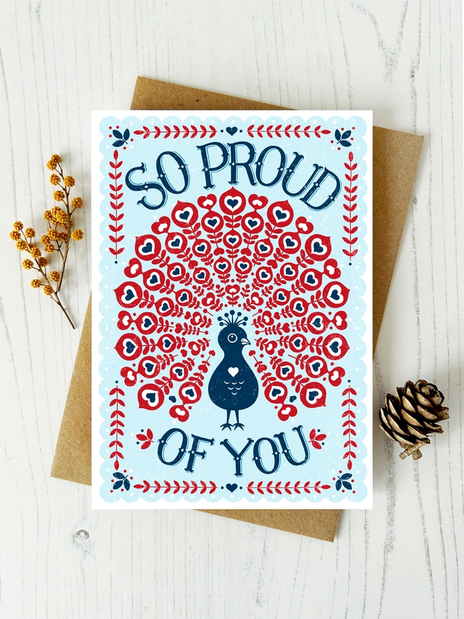 proud of you peacock card in red white and blue with flowers and cone