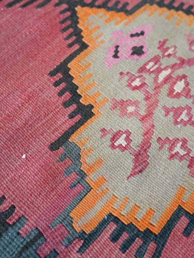 Orangey, red and black geometric vintage kilim hand woven rug on wooden floor in maximalist dining room with green woodwork