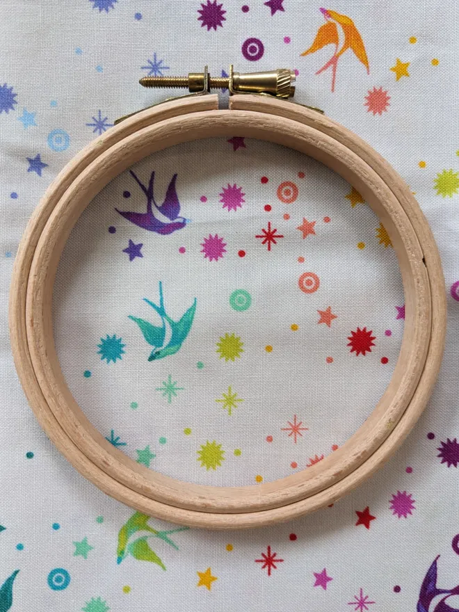 A wooden embroidery hoop lying on fabric with a stars and birds design