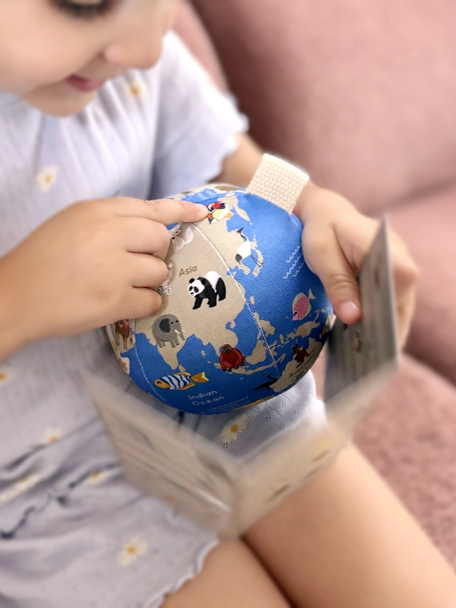 Girl holding first globe soft toy and the guide that comes with it. She is pointing at a Mandarin Duck on the globe