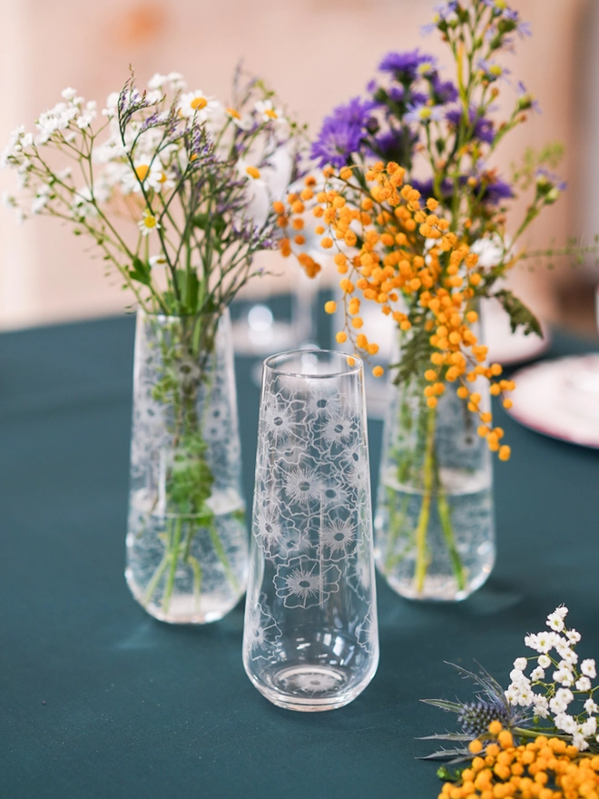 Floral Twist crystal bud vase holding colourful wildflower arrangements placed on a dark green tablecloth.