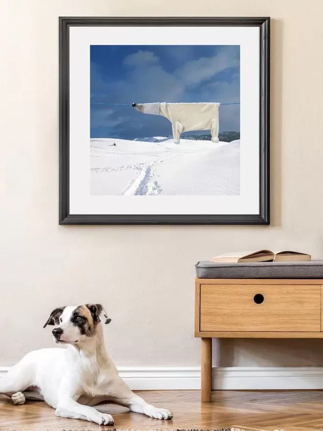 Polar bear made from clothes hung on a clothes line above a snowy scene with a snow track underneath seen with a dog infront.