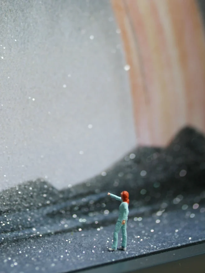 Close up from a miniature scene in an artbox showing a tiny David Bowie looking back at a sparkling cosmic northern lights backdrop.