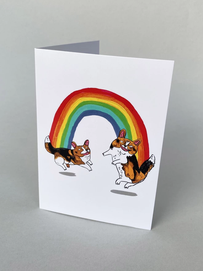 Illustrated rainbow with two dancing corgi's on each end of the rainbow on an A6 Greeting card