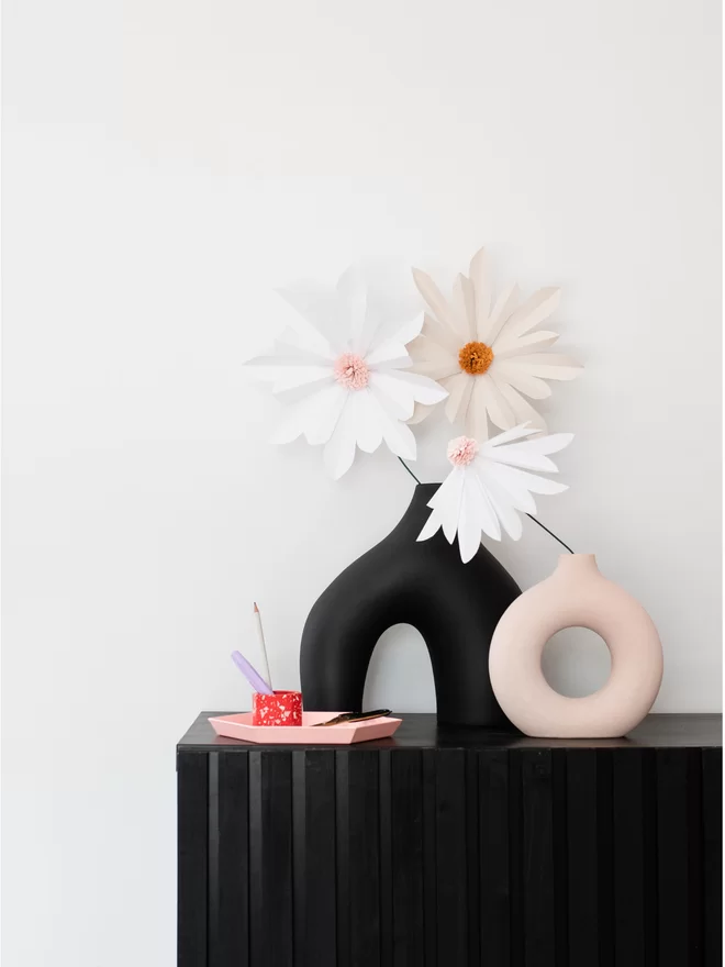 3 giant paper daisies on a black side cabinet, in abstract vases.
