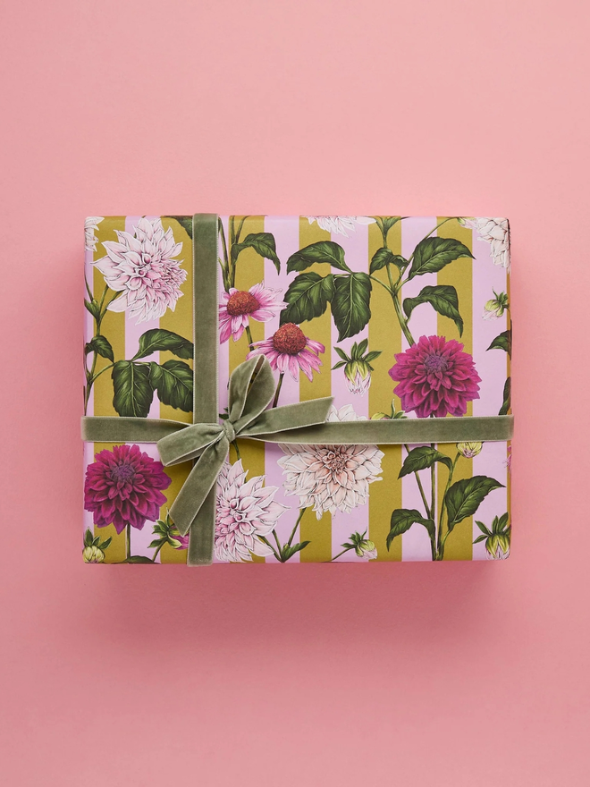 floral riot gift wrap sheet. a box wrapped in pink illustrated floral gift wrap with a green ribbon.