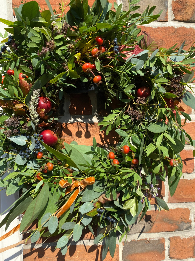 Autumn Hedgerow Wreath with Berries, Herbs, Foliage and Rosehips. Brick background