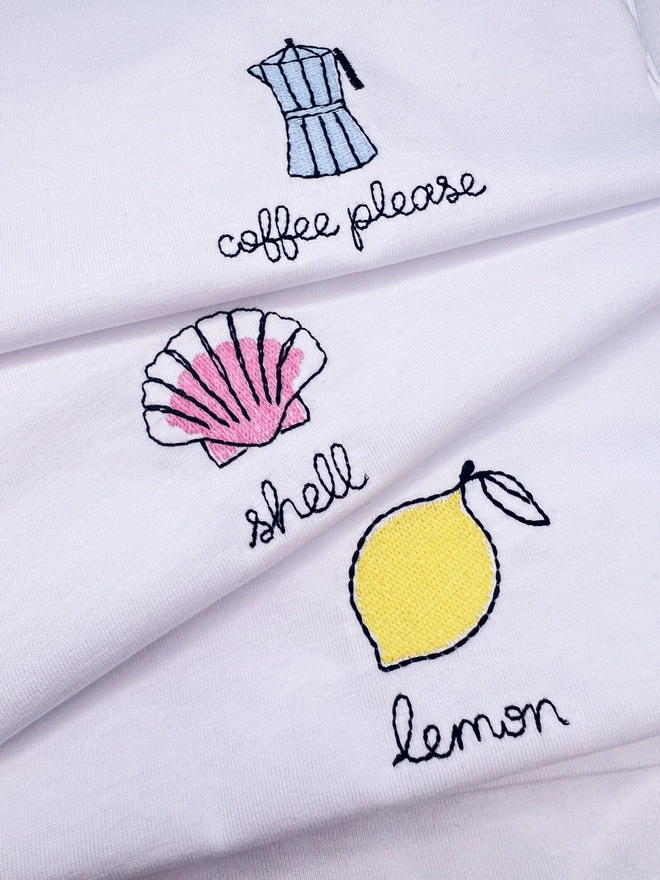     Close-up showing embroidered moka pot, shell and lemon motifs on white T-shirts