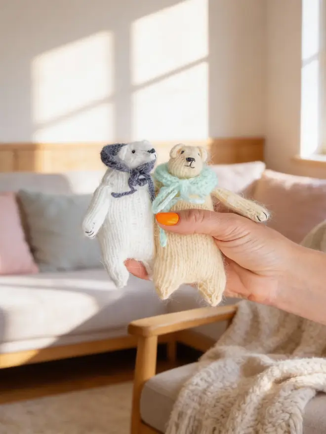 Ottilie The Bear Cashmere Figure, a pair of cashmere bears held by a person against a living room backdrop. 