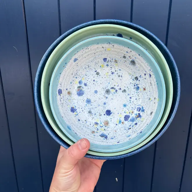 Shoreline Serving Bowls (Set Of 3), a person holding a collection of colourful serving bowls against a navy blue backdrop. 