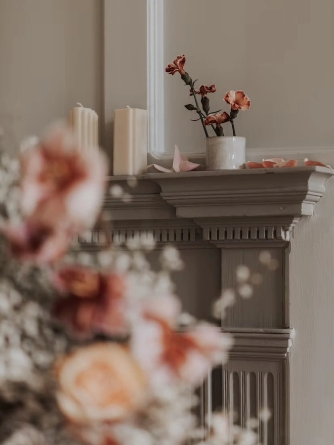 Ikebana, ceramic vase pictured with pink flowers on a ledge, with more flowers on a table next to it. 