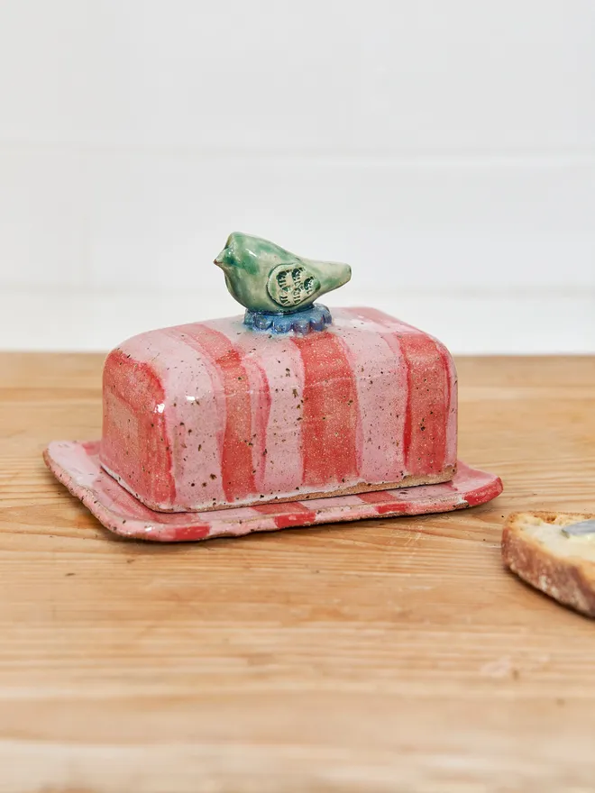 Bird pink and red striped butter dish on a wood surface 