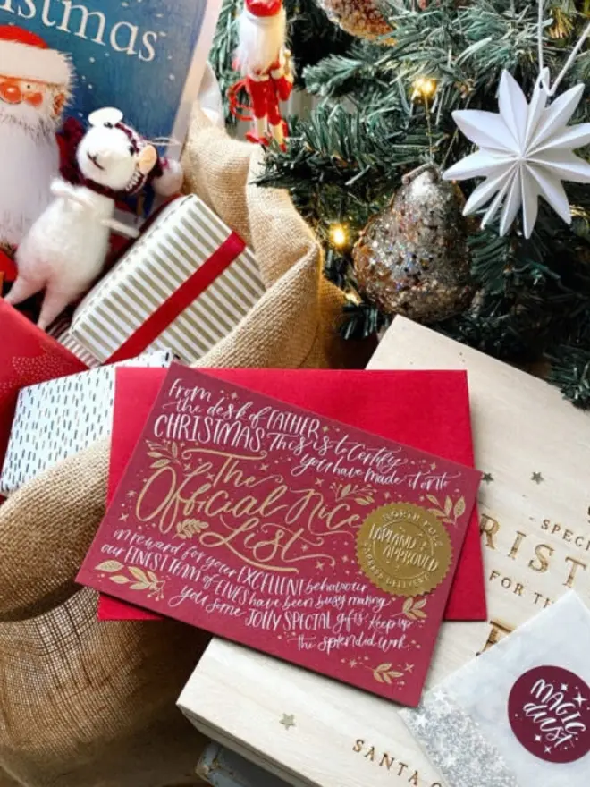 A red certificate with a gold seal, resting on a Christmas Eve box beneath a decorated tree.