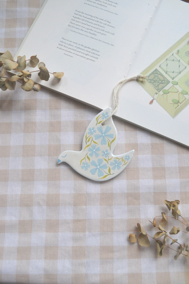 white ceramic hanging bird with blue and green floral designs, in front of gingham 