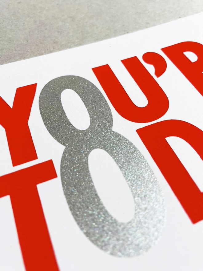 Close up of the screenprinted red and silver ink, showcasing the 8 which is made from the O letters of other words. The silver sheen is glistening.