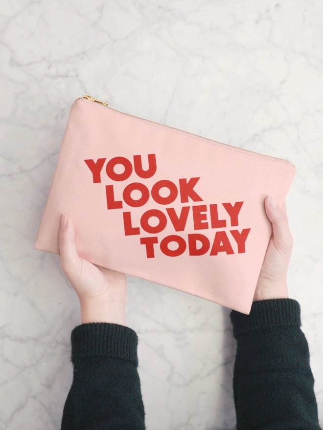 two hands holding out a blush pink canvas zip pouch with the words you look lovely today 