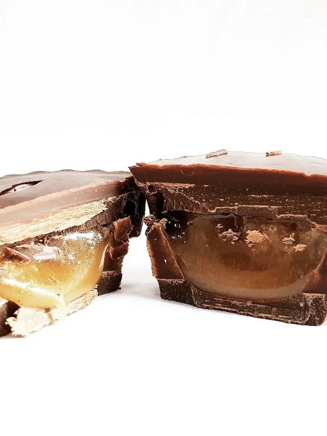 Vegan Irish Sea Salt Chocolate Caramel Cups 60% (Box Of 4), a chocolate cup split in two sitting on a wooden surface. 