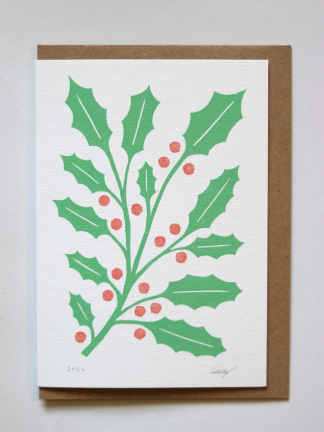 A Christmas card featuring a reproduction of an original linocut print of holly