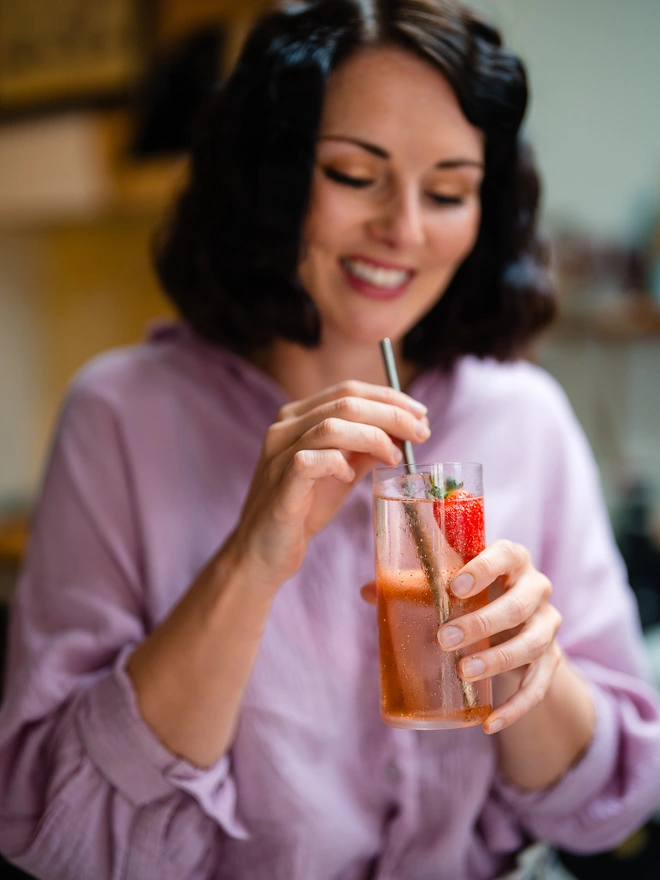 Holly smiling at a glass of strawberry spirit and tonic