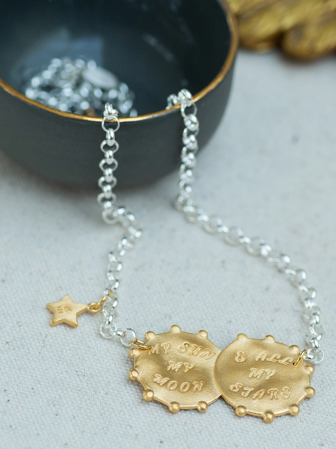 The Lunar Glow Double Coin Necklace is a beautiful celebration of sun and moon energy. Crafted in sterling silver with 18ct gold plate, this tactile mixed metal necklace features heart sunburst and moon-and-stars coins, engraved with “My sun, my moon and all my stars.” Finished with a delicate star charm, it’s a meaningful celestial keepsake designed for everyday wear.