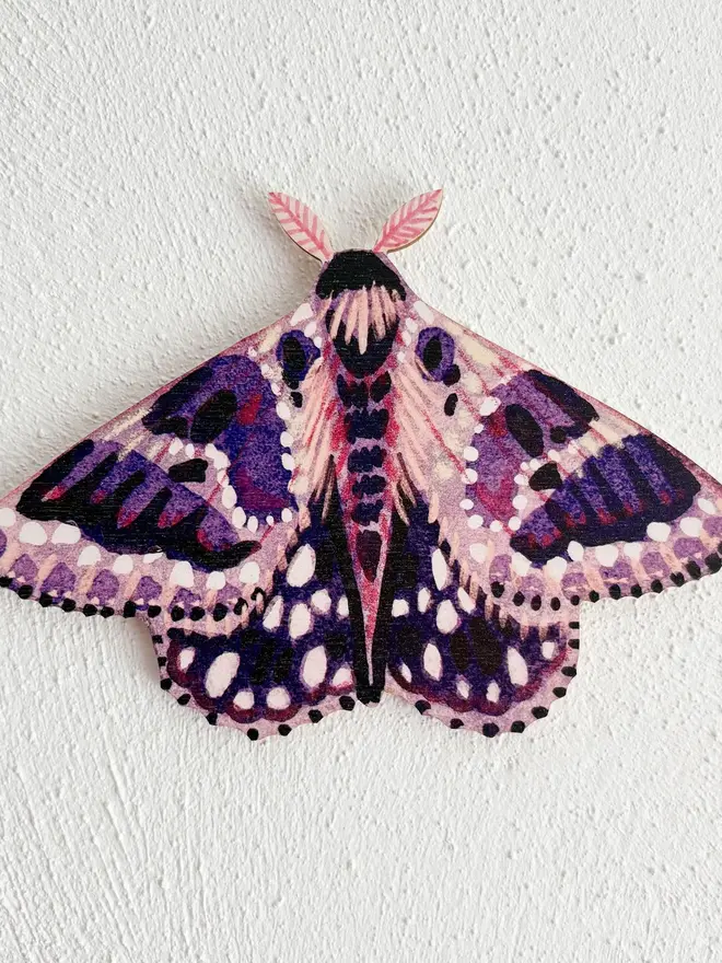 wooden moth wall decoration. purple wooden moth hung on plain white wall.