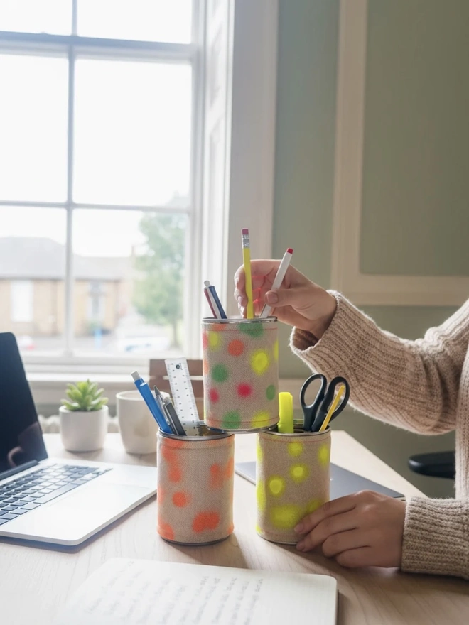 Upcycled & Repurposed Linen Tin Holder Polka Dot Print, a trio of polka dot tins on a desk accompanied by other study items. 
