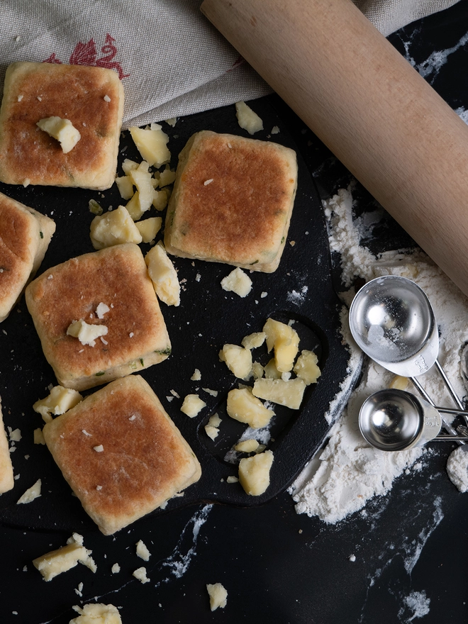 Cheese and Leek Welsh Cakes on a griddle with broken cheese and flour