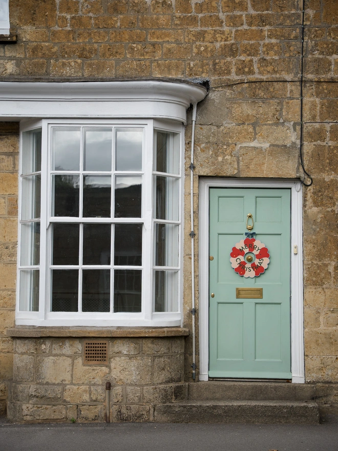 Red and pale pink Hand painted Christmas Wreath with gold leaf stars on a pale green front door