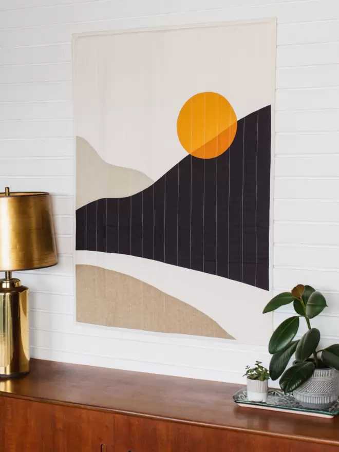 Sun Road Quilt Hanging On A Wall Above Wooden Furniture