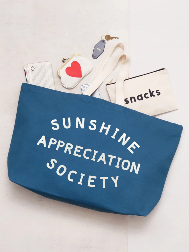 Blue oversized sunshine appreciation society slogan tote bag laying on the floor with items spilling out 