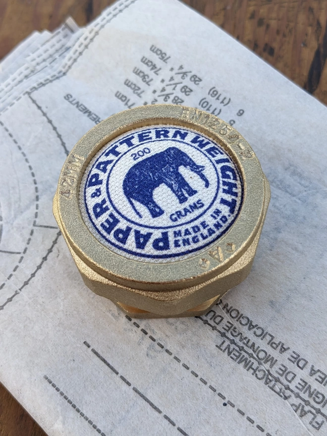 Blue elephant brass pattern & paper weight lying on a sewing pattern