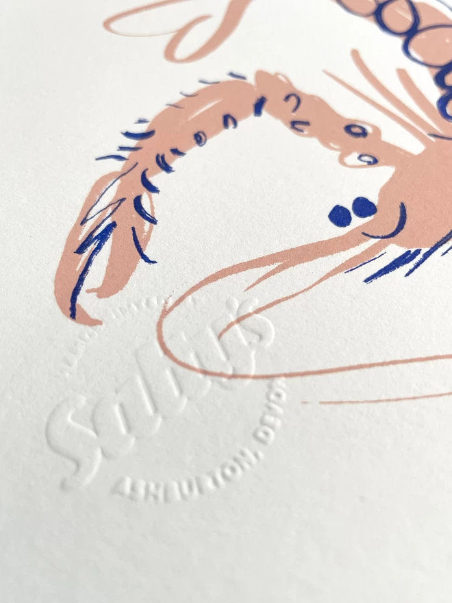 Close up of an embossed Salty’s logo, saying handprinted in Ashburton, overlapped with the face and claw of a screenprinted langoustine.