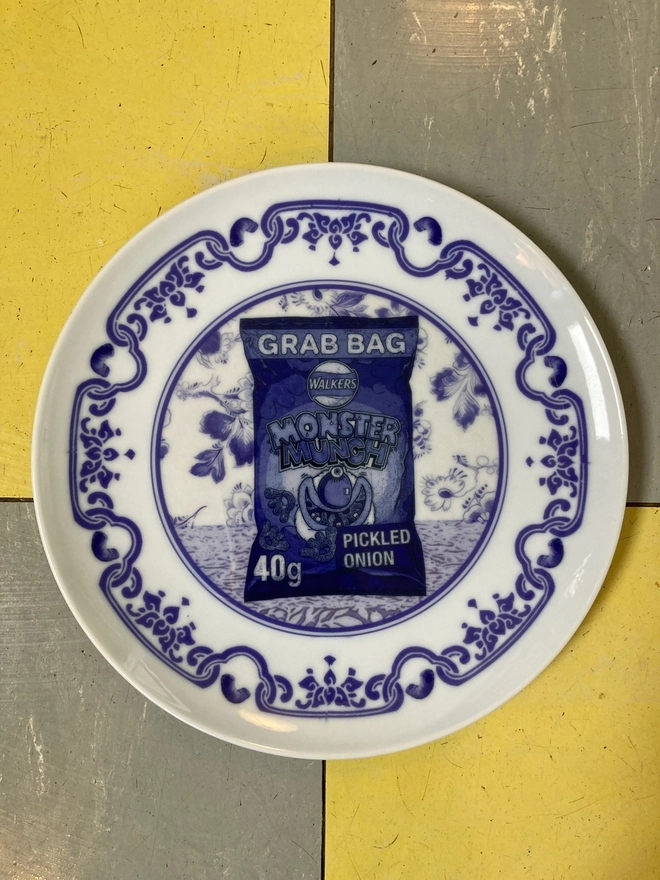 An 8" blue and white 'Delft' style plate featuring a packet of Monster Munch