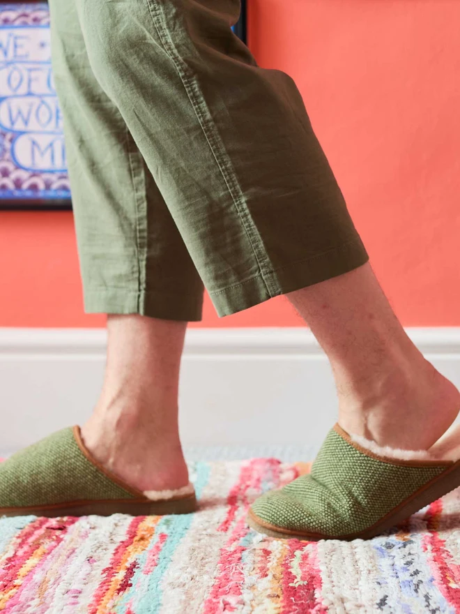 MAN WALKING IN GREEN CHECKED SLIPPERS IN FRONT OF A CORAL WALL