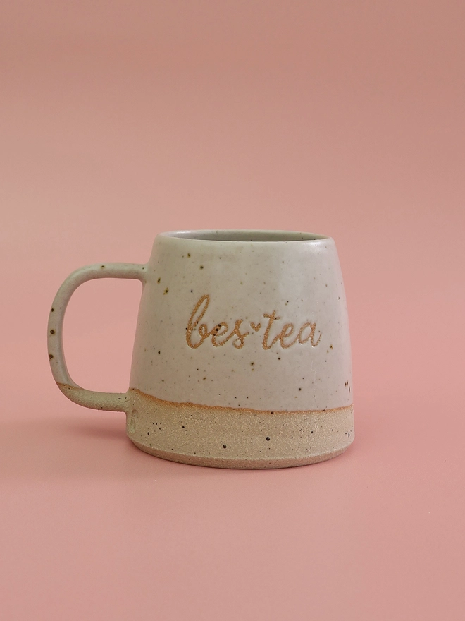 bes-tea saying on the front of a white handmade ceramic mug, sitting on a pink background