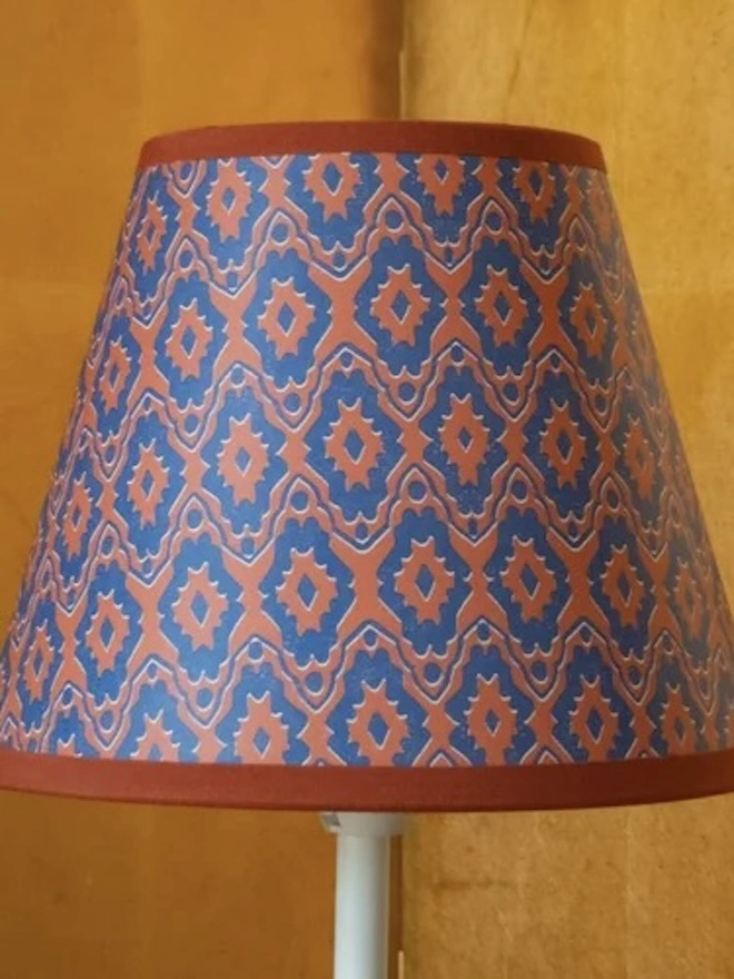 Candle Clip Shades. A small tapered lampshade in a rust and blue geometric ikat-style block print with a rust trim. The richly patterned shade brings warmth and character to a side table lamp or wall light.
